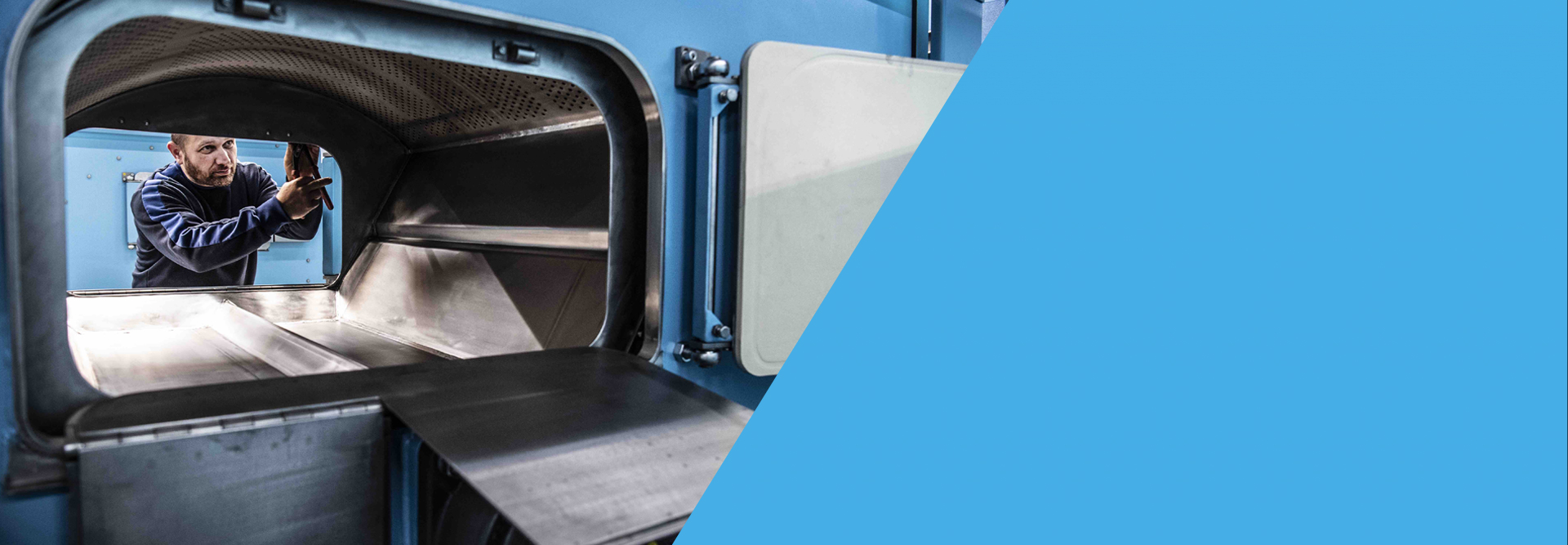 Technician at the open door of a Unica washer-extractor, the perforated drum and the divided pocket visible inside